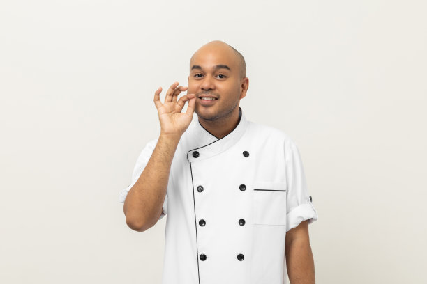 快乐年轻英俊的亚洲男子厨师在制服站岗好味道高兴美味的手势。烹饪印度人职业厨师或面包师在厨房餐厅和酒店。图片下载