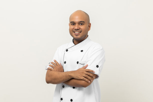 微笑的年轻英俊的亚洲男子厨师制服站姿势手臂交叉看着镜头在孤立的背景。厨师职业厨师或面包师在厨房、餐厅和酒店工作的人。图片下载