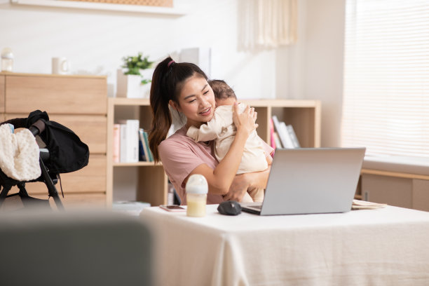 妈妈抱着小男孩，一边用手提电脑工作。这个天真无邪的婴儿把头靠在妈妈身上，他们互相依偎着。妈妈和孩子坐在舒适的工作室里。图片下载