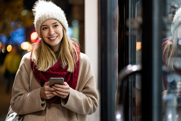 年轻美丽的女人用她的手机上网在冬天的一天在城市图片下载