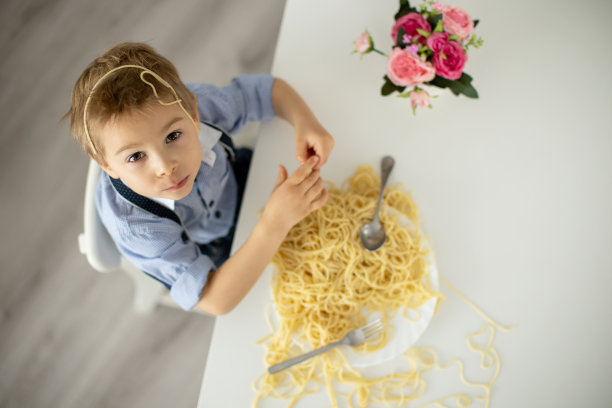 可爱的学前班孩子，金发男孩，在家吃意大利面，把家里弄得一团糟图片下载