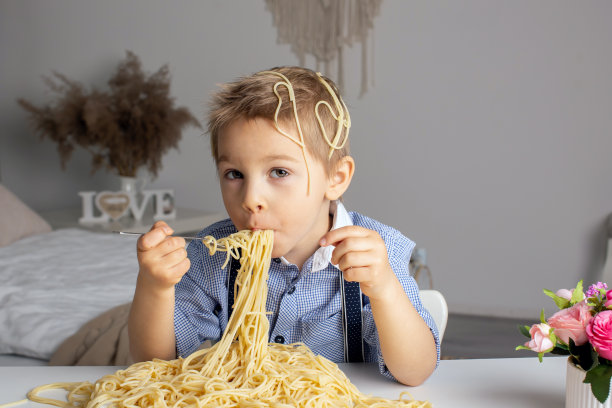 可爱的学前班孩子，金发男孩，在家吃意大利面，把家里弄得一团糟图片下载