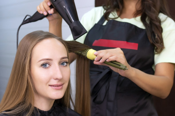 女理发师，美容院。用吹风机和圆刷吹干头发。图片下载