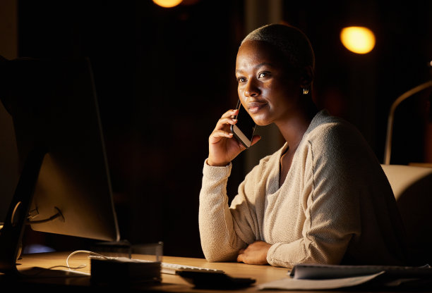 这张照片拍摄的是一位年轻的女商人，晚上在办公室的电脑上用手机聊天图片下载