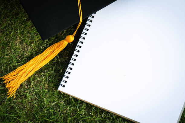 黑色的毕业帽和笔记本放在绿色的草地上图片下载