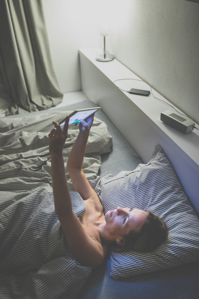 一位中年妇女在晚上睡觉前使用她的平板电脑图片下载