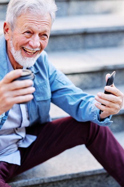 一个笑得很开心的老男人正坐在户外的楼梯上，在电话里调情。图片下载