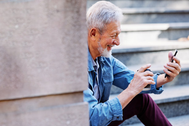 一个笑得很开心的老男人正坐在户外的楼梯上，在电话里调情。图片下载