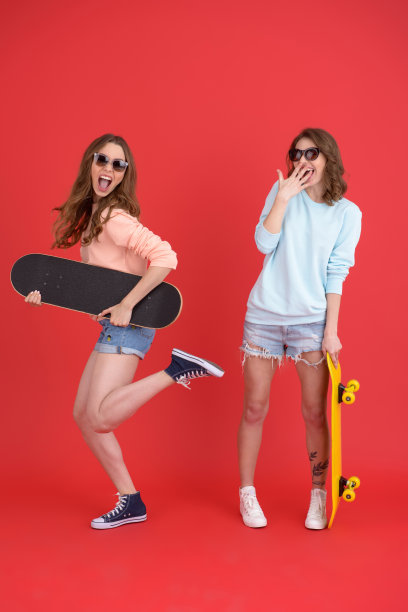 年轻快乐的两位女士朋友拿着滑板。图片下载