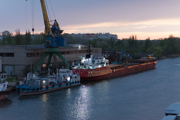 在一天结束的时候，起重机在货港的背景下将废金属装载到货船上图片下载