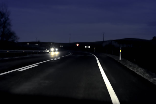 夜间的道路照片，在夜间有一个向左的曲线和车辆行驶在它的前面。有选择性的重点。图片下载