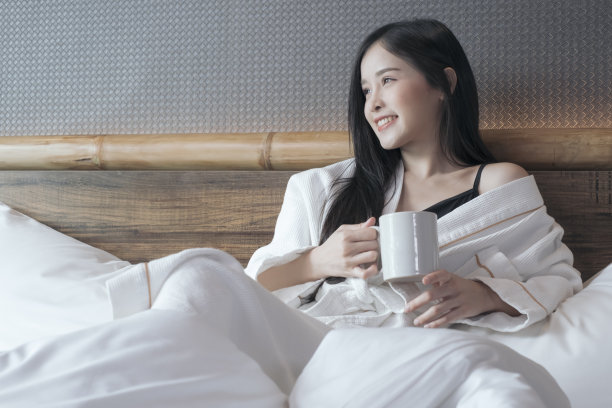 快乐美丽的年轻亚洲妇女放松地喝和看着一杯热咖啡或茶在早上的床上。图片下载