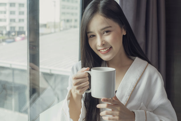 快乐美丽的年轻亚洲妇女放松地喝和看着一杯热咖啡或茶在早上。图片下载