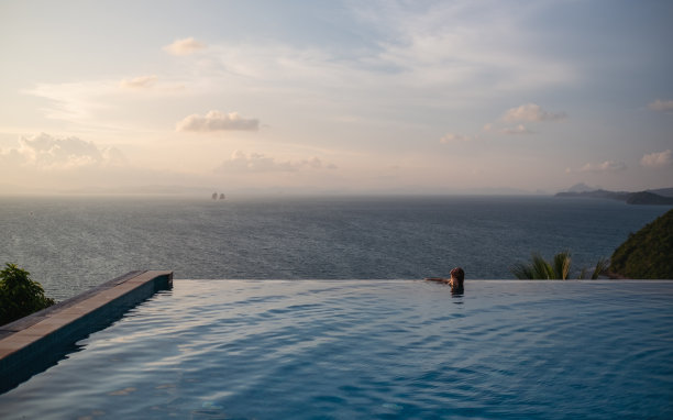 一个年轻的女人放松在无限的游泳池，看着美丽的日落和海景图片下载