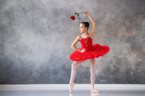 一个可爱的小女孩梦想成为一名职业芭蕾舞演员。一个女孩穿着鲜红色的芭蕾舞裙，脚穿尖头鞋，在大厅里跳舞。职业学校的学生。图片下载
