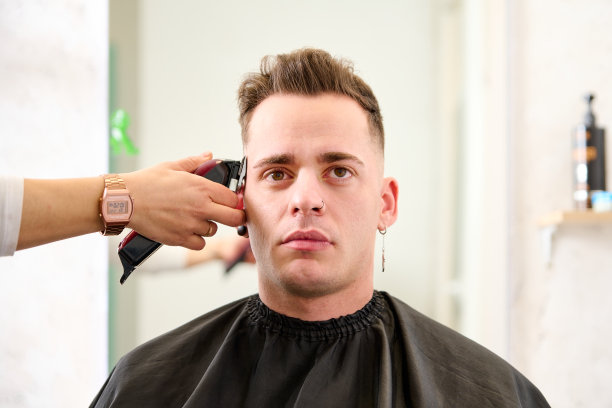 一个男人坐在理发店里，理发师正在用电剪给他理发图片下载