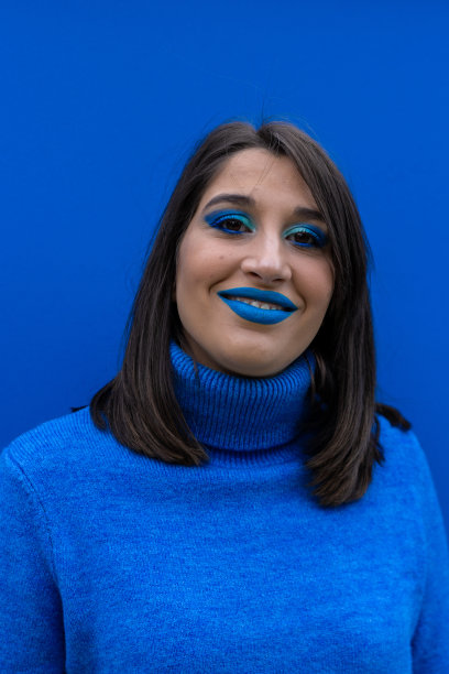 垂直特写欢快的年轻女子与蓝色眼影化妆。美丽的肖像女模特与生动的化妆笑在蓝色的背景。图片下载