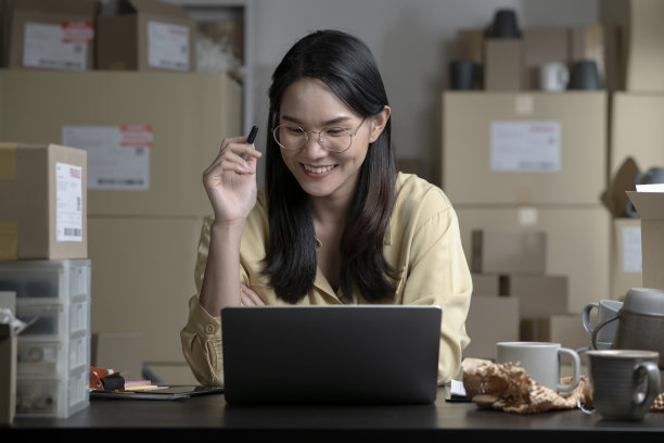 年轻的亚洲女网上卖家微笑着记录着顾客的订单。图片下载