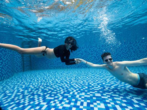 穿着泳衣、戴着太阳镜的年轻男女在水下手牵手微笑。图片下载