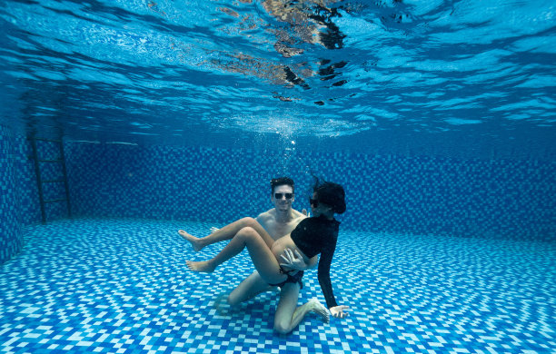 一对怀孕夫妇在蓝色的游泳池水下拍摄独特的孕妇照。图片下载