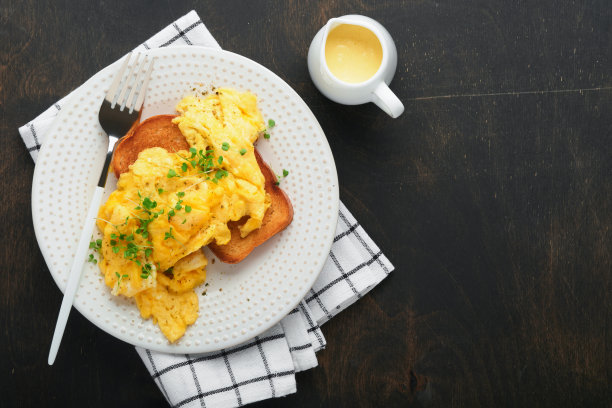炒鸡蛋。松软黄油炒蛋面包配微绿萝卜和荷兰酱，白色盘子，深色的旧木头背景。自制早餐或早午餐。前视图。图片下载
