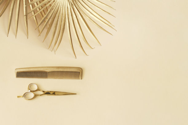 金色的理发剪刀和梳子在黄色的背景上。发廊饰品和装饰叶。图片下载