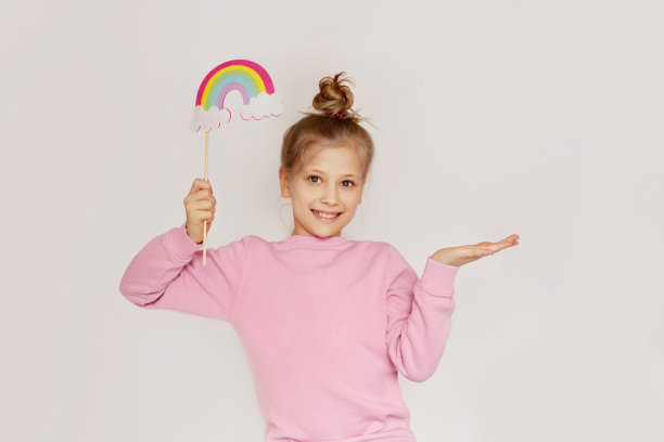 一个快乐的女孩在用毛毡做成的云朵上拿着彩虹。春天的肖像在一个轻的背景与文本空间。复活节的概念图片下载