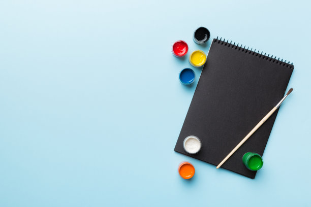 相册页和油漆，铅笔，画笔上的彩色背景。顶部视图与空的空间。工作场所的创造力。家庭教学概念图图片下载