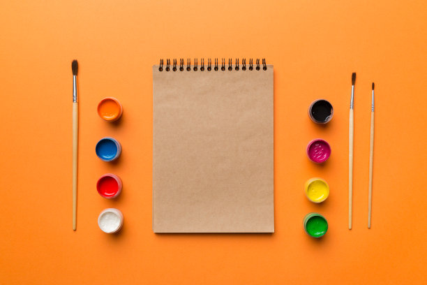 相册页和油漆，铅笔，画笔上的彩色背景。顶部视图与空的空间。工作场所的创造力。家庭教学概念图图片下载