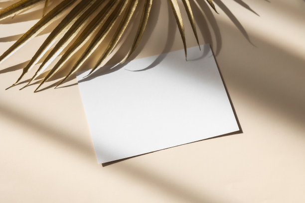 邀请卡模型与金黄色棕榈叶在米色柔和的背景。俯视图，平躺，复制空间。模板空白的白纸模拟为品牌和广告图片下载