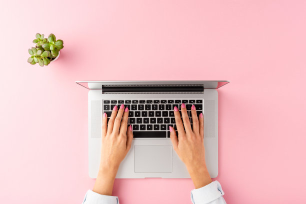 头顶的照片，一个女人的手在粉红色的桌子上用笔记本电脑。办公桌面。平躺图片下载