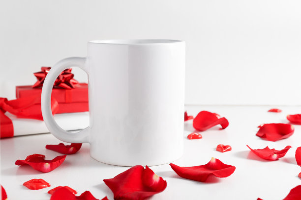 白色咖啡杯，礼品盒和红色玫瑰花瓣放在木桌上。杯子模型与复制空间，假日概念。图片下载