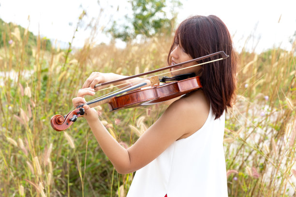美丽的亚洲女人拿着小提琴，站在草地上，心情愉快。图片下载