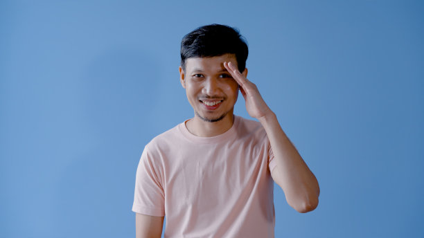 亚洲男人的胡子，年轻人的一半脸是严厉和严肃的寻找什么。，蓝色背景上的孤立的室内工作室。图片下载