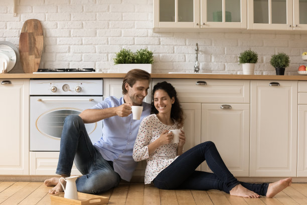 年轻夫妇端着杯子坐在厨房的木地板上图片下载