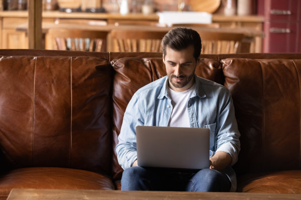 专注的千禧一代男性坐在舒适的沙发上使用现代笔记本电脑图片下载