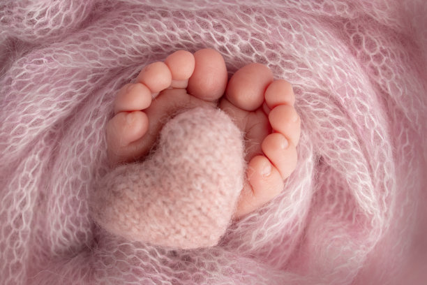 新生婴儿的小脚。粉红色毯子里新生儿柔软的脚。新生儿的脚趾，脚跟和脚的特写。在婴儿的腿上编织着粉红色的心。微距摄影工作室图片下载