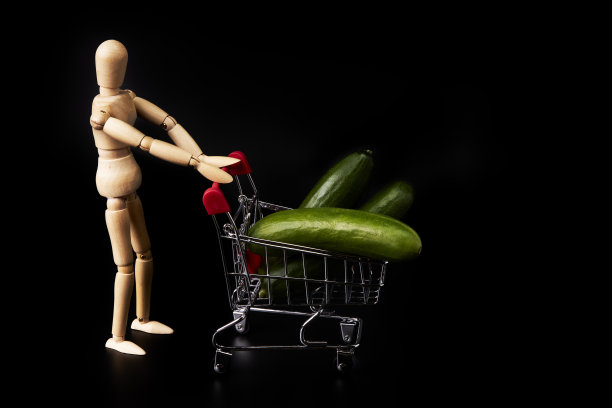 假人推着购物车，黑色背景上放着黄瓜。健康的购物图片下载