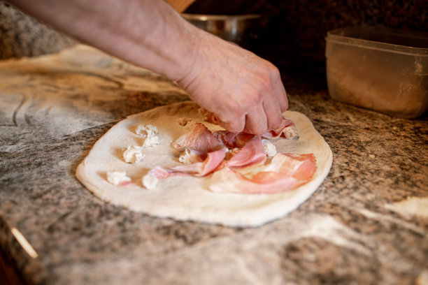 把培根片和马苏里拉奶酪片放在厨房柜台上的披萨面团上图片下载