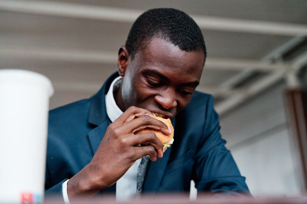 非洲裔美国商人咬着新鲜美味的汉堡，看着镜头。图片下载