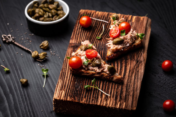 开胃菜意式烤面包配金枪鱼。意式意式烤面包三明治配金枪鱼罐头，番茄和刺山柑。烤金枪鱼，黑色背景，俯视图，平躺图片下载