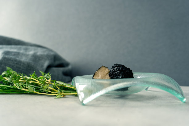 刚切好的黑松露放在一个小玻璃碗里。附近是草本植物(迷迭香，百里香)。灰色的墙上，浅灰色的桌子上放着一只碗。图片下载