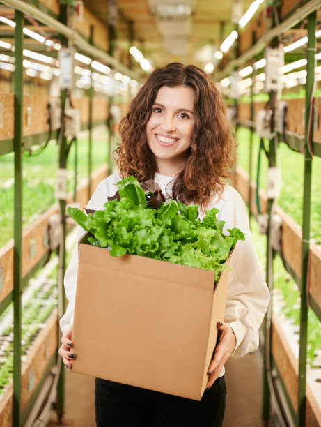 快乐的女人拿着装满新鲜绿叶蔬菜的盒子。图片下载