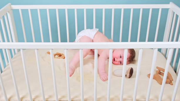 快乐的婴儿宝宝躺在婴儿床上，画室蓝色的背景。穿着白色尿布微笑的孩子图片下载