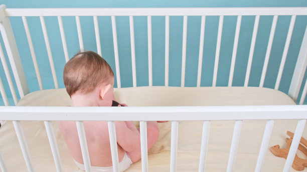 小男孩坐在婴儿床上玩玩具，蓝色的画室背景。穿着白色尿布的白人小孩图片下载