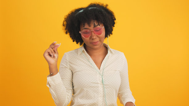 快乐迷人的非洲年轻女子跳舞孤立在黄色的背景上。开朗漂亮的女孩快乐的平板电脑笔记本网上音乐微笑和移动的身体跟着音乐积极。图片下载