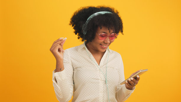 快乐迷人的非洲年轻女子跳舞孤立在黄色的背景上。开朗漂亮的女孩快乐的平板电脑笔记本网上音乐微笑和移动的身体跟着音乐积极。图片下载