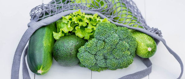一个带绿色蔬菜在一个白色木制背景的特写线袋。健康的饮食食品。健康营养、素食、生态的理念。拒绝使用塑料袋。图片下载