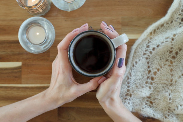 女人的手拿着一杯热饮，站在木桌上，蜡烛和温暖的格子花呢，舒适的家周末，冬天，秋天秋天的概念图片下载