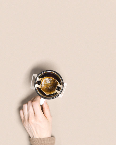 女人手握咖啡杯与黑咖啡饮料，滴滤咖啡袋与咖啡粉冲泡在杯子，纸袋滴滤咖啡，米色背景，俯视图，最小的平面，柔和的颜色图片下载